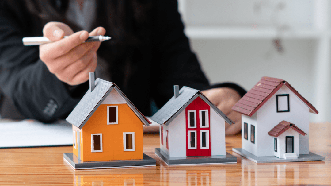 A real estate agent presents three model houses on a desk, highlighting options for a potential buyer.